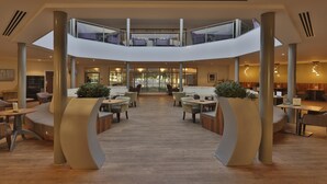 Een ruime lobby met een centraal atrium, zithoeken en een tussenverdieping.