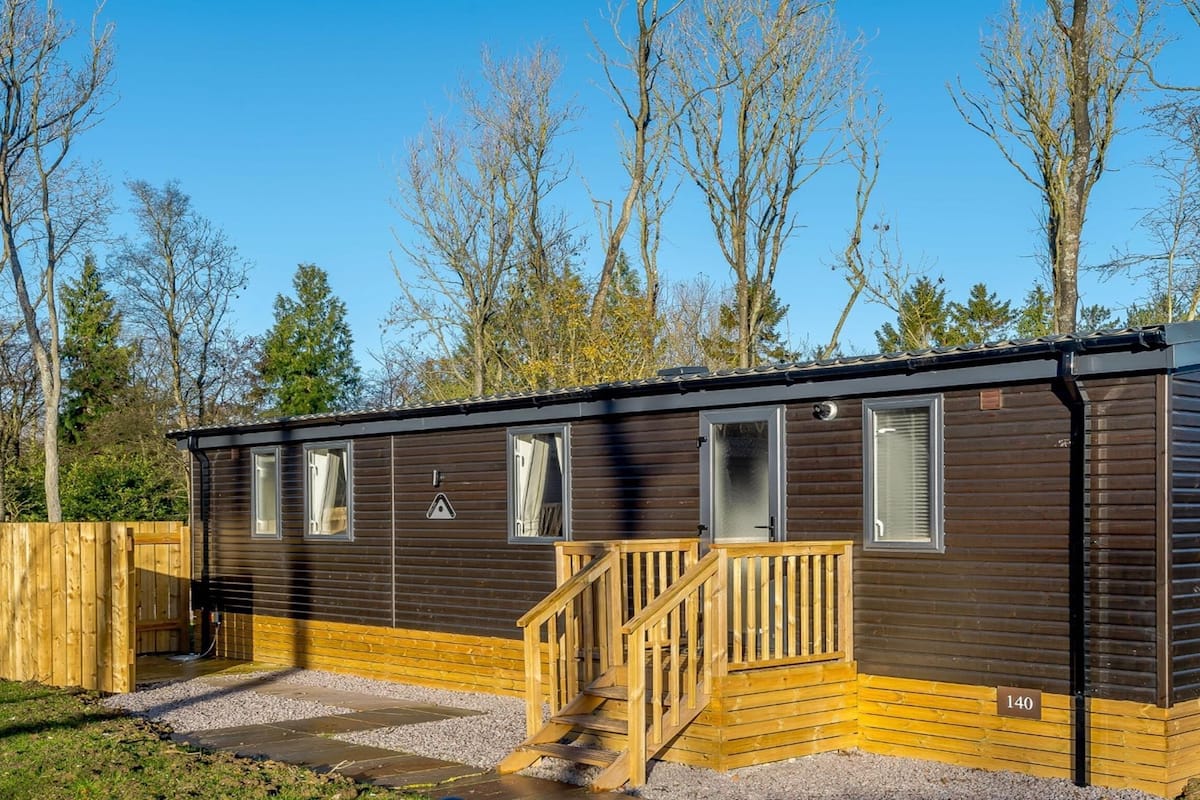 Een compacte, gelijkvloerse blokhut met een houten terras en een kleine trap naar de ingang.