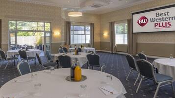 Een congreszaal met ronde tafels, stoelen en een projectiescherm waarop 'Best Western PLUS' staat.