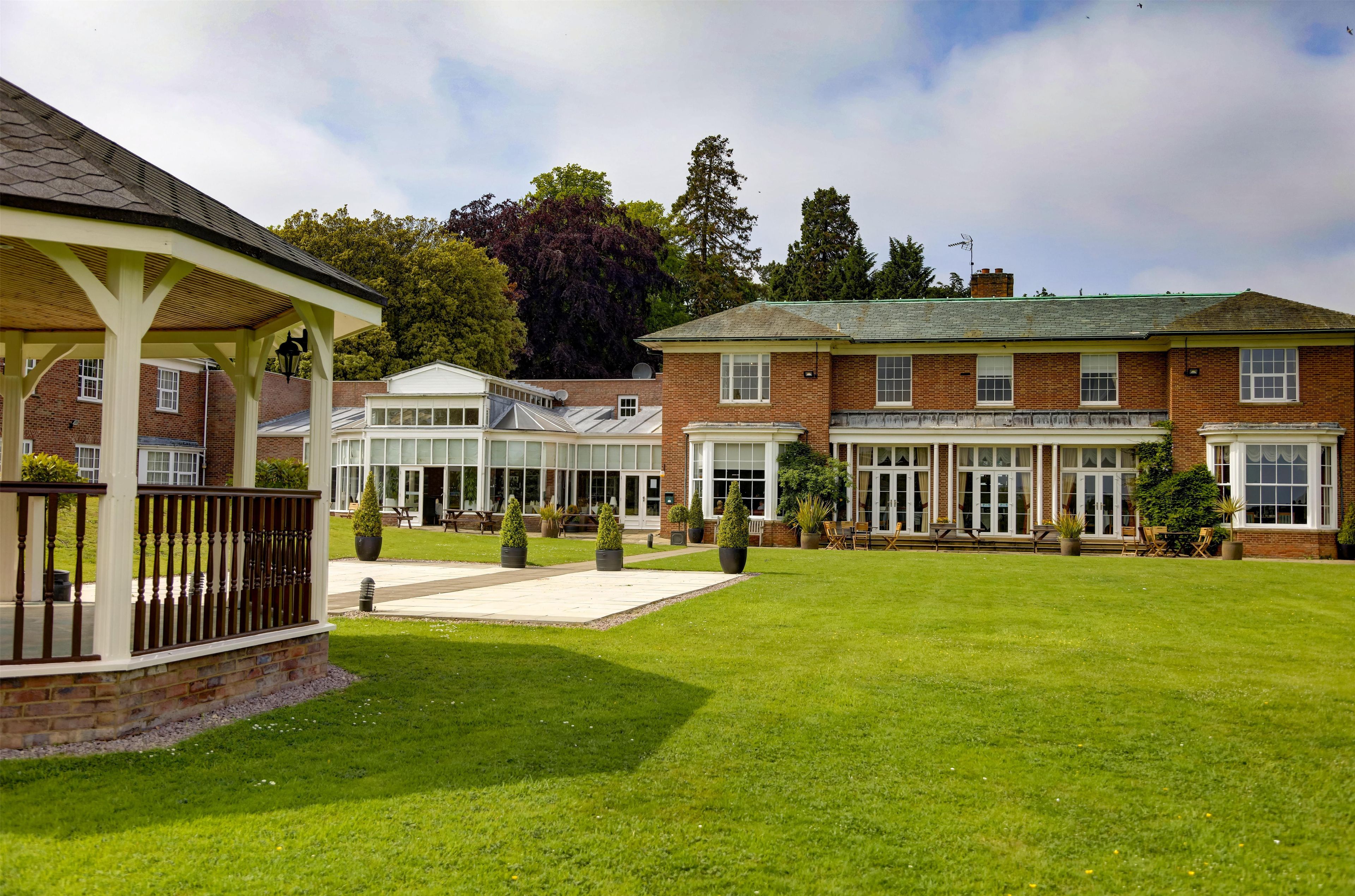 A building with a covered patio area, a lawn, and a brick facade.