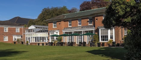 A large brick building with a covered outdoor seating area, multiple windows, and a well-maintained lawn.