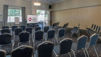 Un salón de conferencias con filas de sillas, una pantalla de proyector y un cartel que dice "Best Western PLUS".