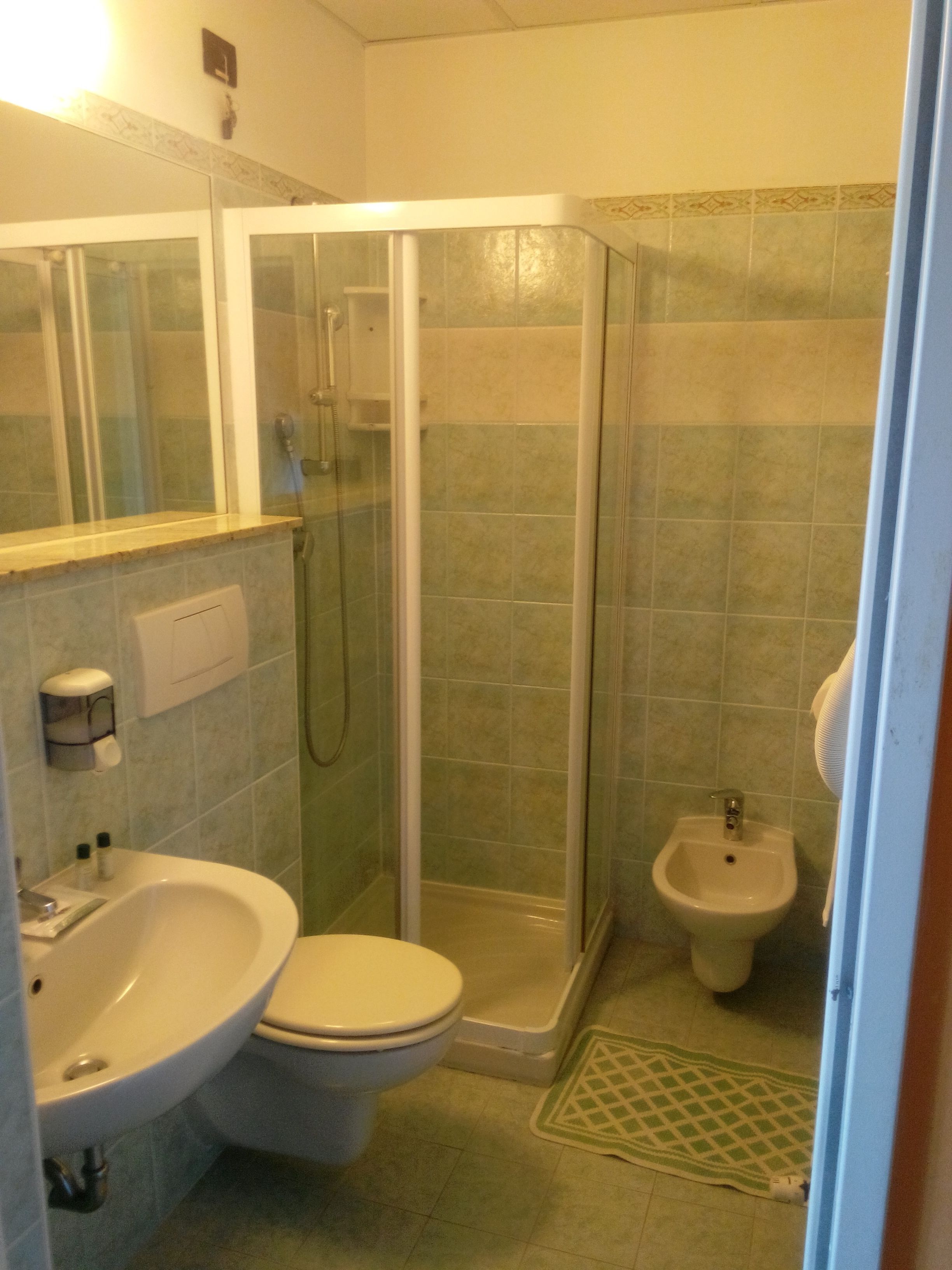 Un bagno con doccia vetrocamera, WC, bidet e lavandino.
