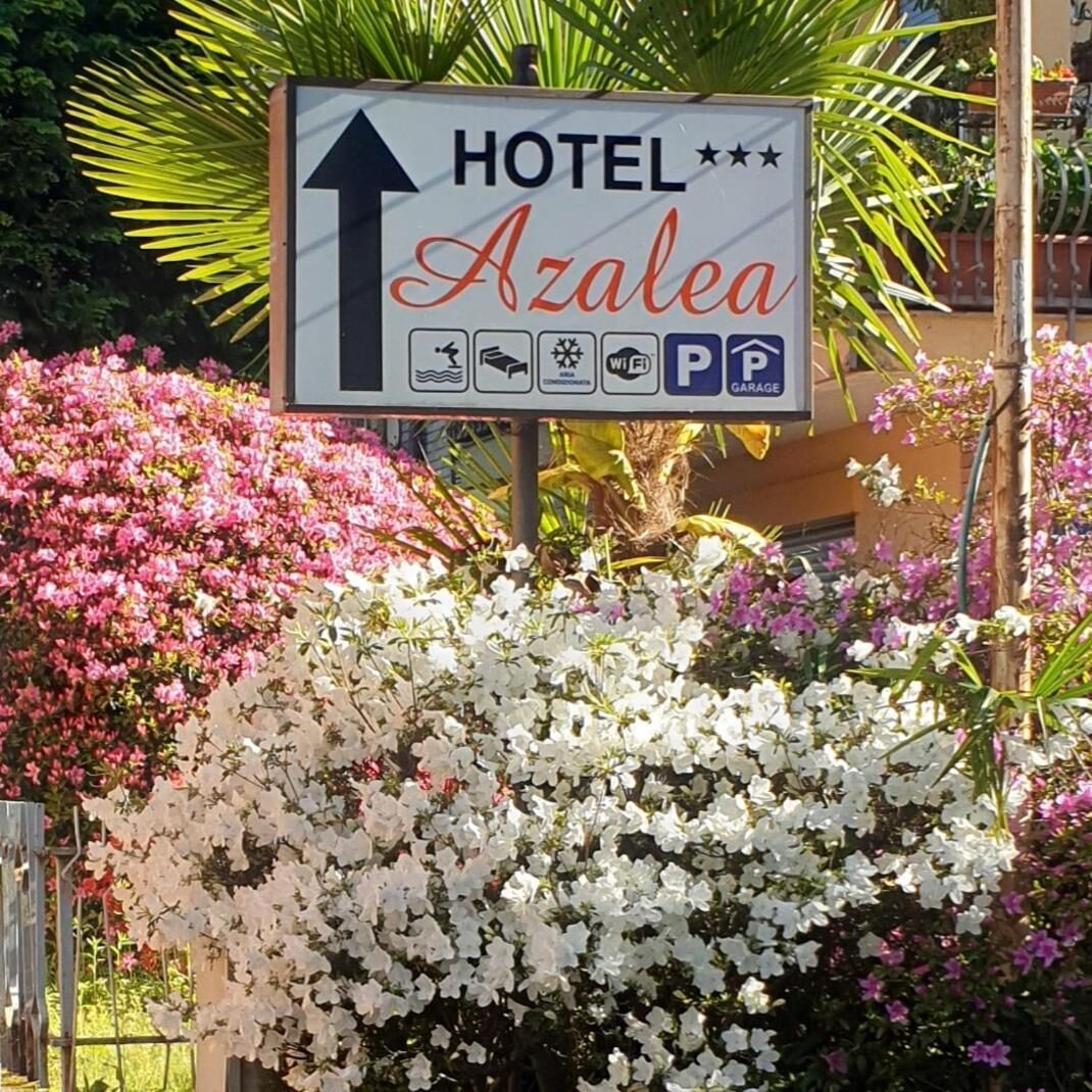 Een hotelschilt met pictogrammen voor voorzieningen, waaronder een parkeersymbool, omringd door bloeiende planten.