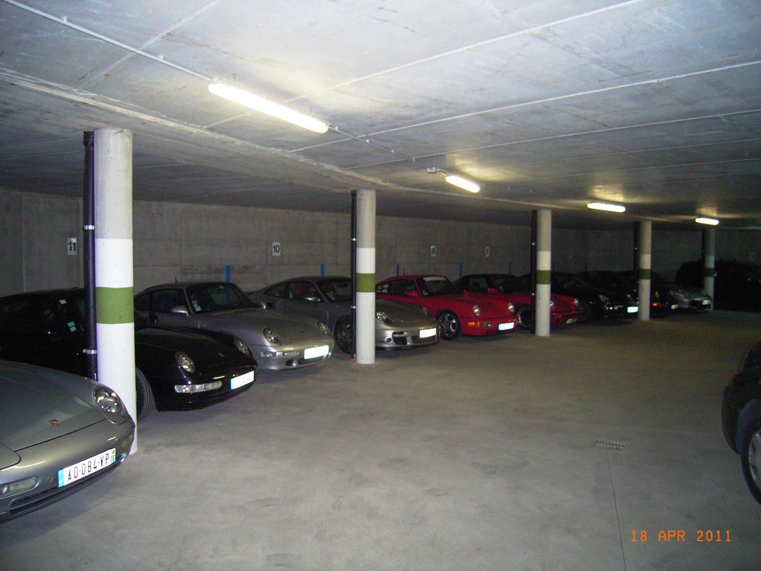 Een parkeergarage met meerdere auto's die in rijen staan, betonnen pilaren en fluorescent verlichting.