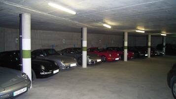 Een parkeergarage met meerdere auto's die in rijen staan, betonnen pilaren en fluorescent verlichting.