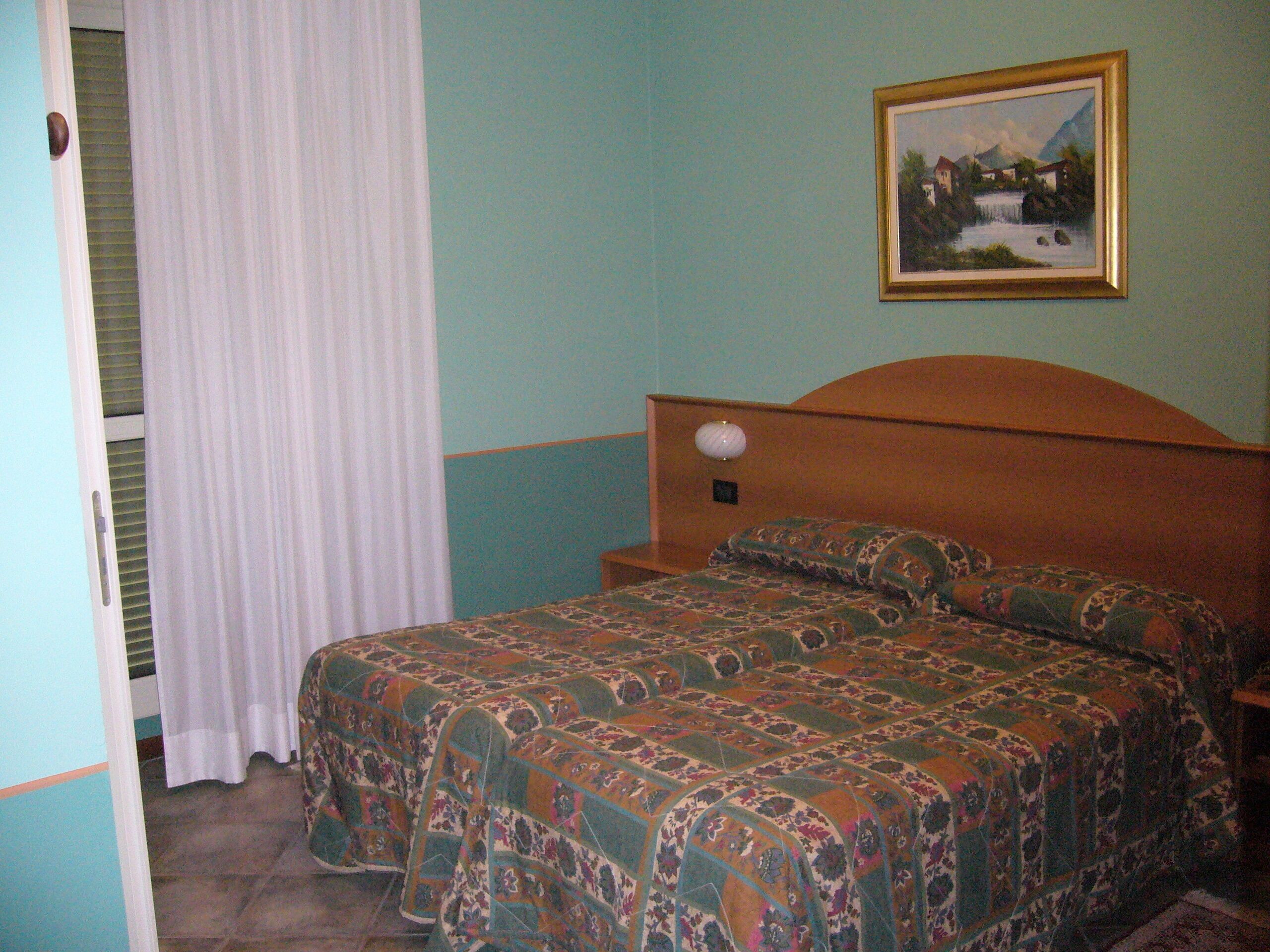 A bedroom with a bed, a nightstand, a lamp, and a painting on the wall.