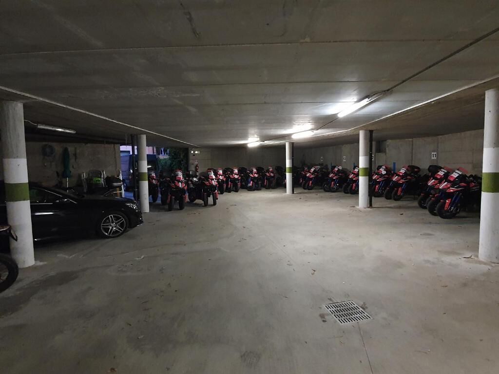 Een parkeergarage met betonnen pilaren, een zwarte auto en rijen geparkeerde motorfietsen.