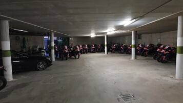 Een parkeergarage met betonnen pilaren, een zwarte auto en rijen geparkeerde motorfietsen.