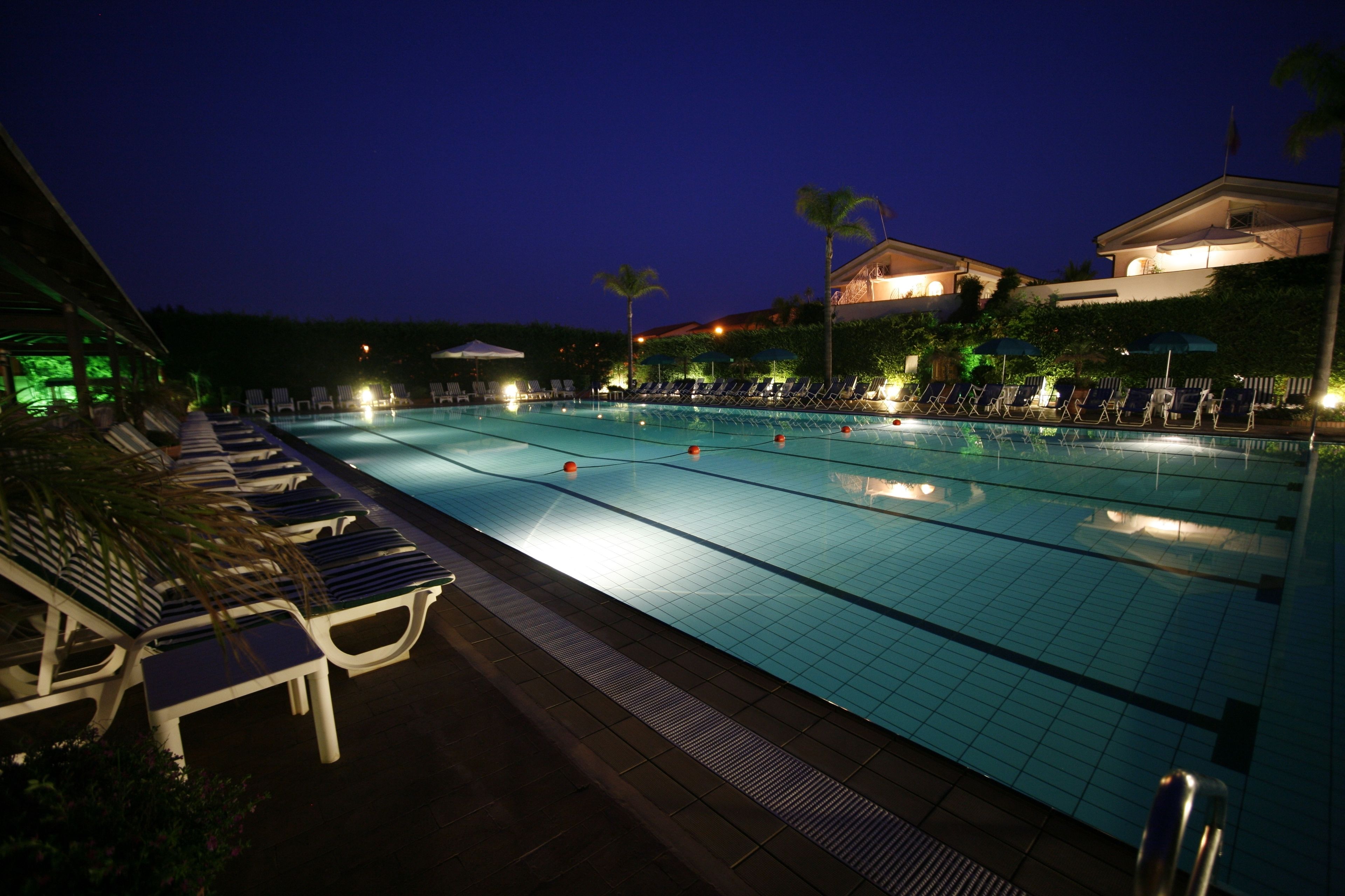 A swimming pool with lounge chairs and umbrellas, surrounded by buildings and palm trees.