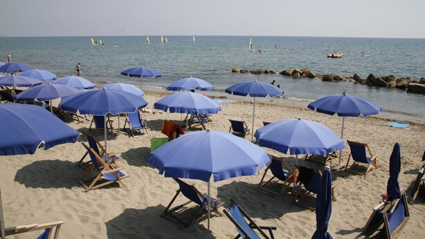 A beach with multiple blue umbrellas and beach chairs.