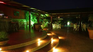 A nighttime outdoor area with a curved brick pathway leading to a seating area with chairs and tables.