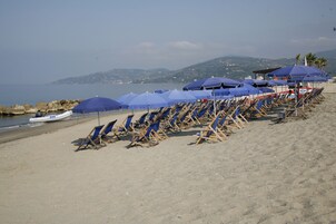 Una playa con hileras de sombrillas azules y sillones de madera orientados al mar.