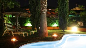 A swimming pool surrounded by palm trees and lounge chairs at night.