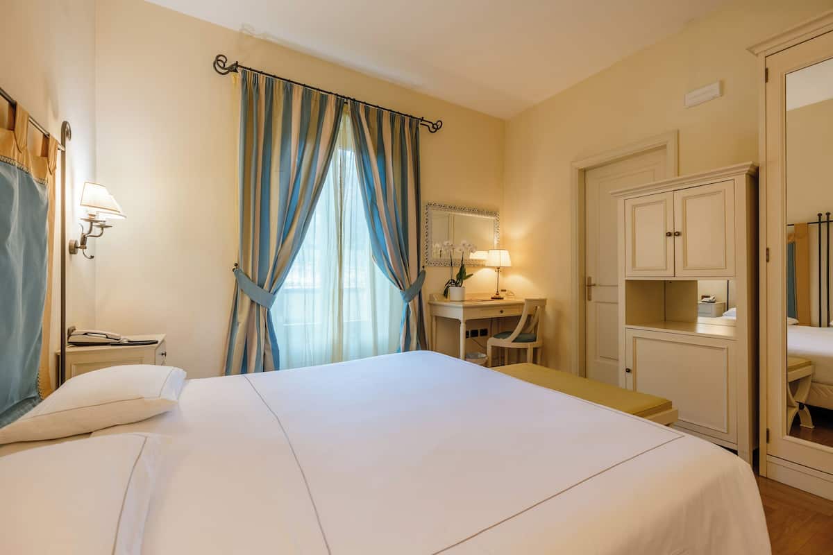 Une chambre d’hôtel avec un grand lit, un bureau avec une chaise, un miroir et une armoire.
