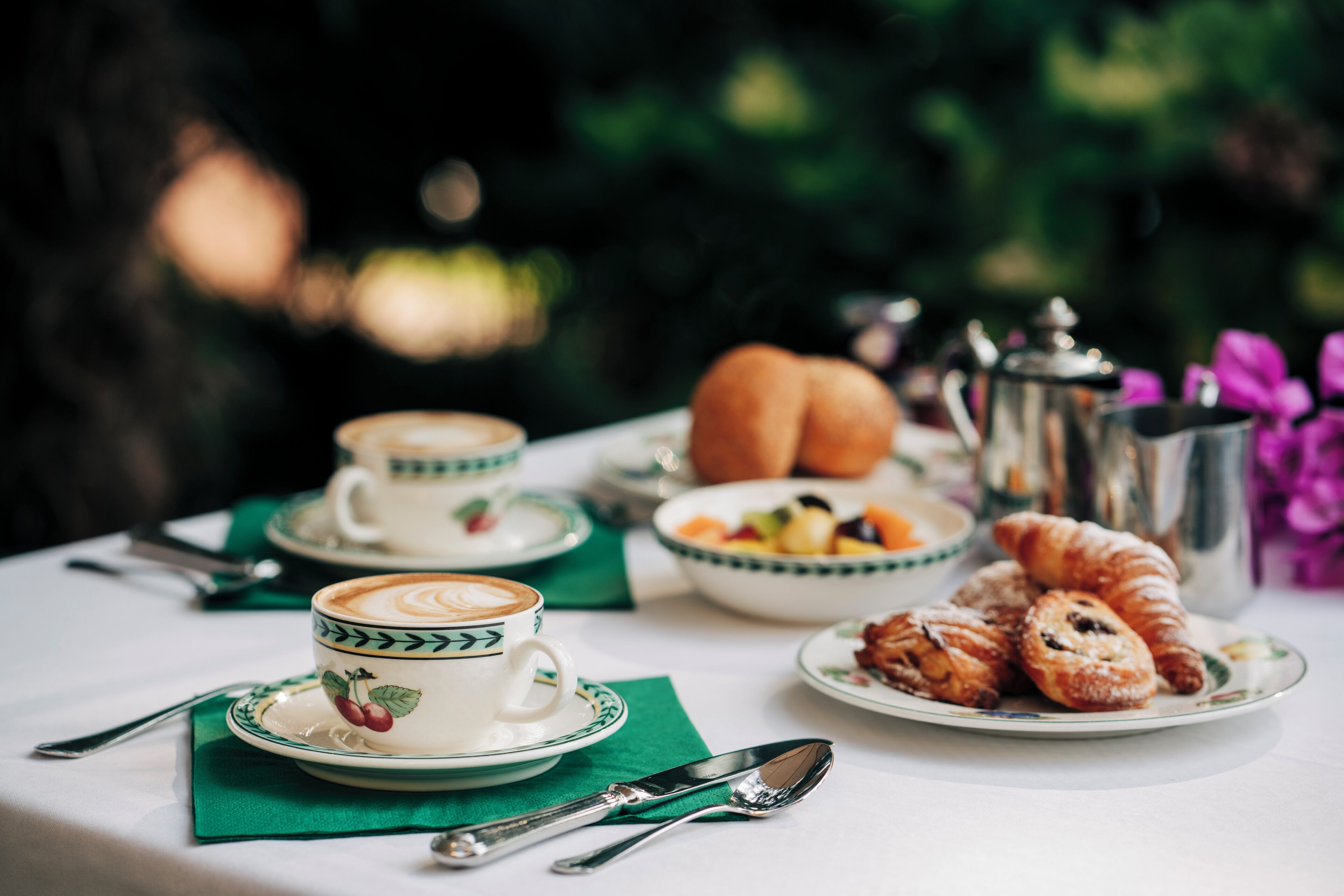 Una mesa dispuesta con una taza de café, croissants, un frutero y una tetera.