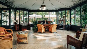 A conservatory with wicker furniture, a chandelier, and large windows offering a view of the outdoors. - Hotel Villa Sofia (Gardone Riviera)