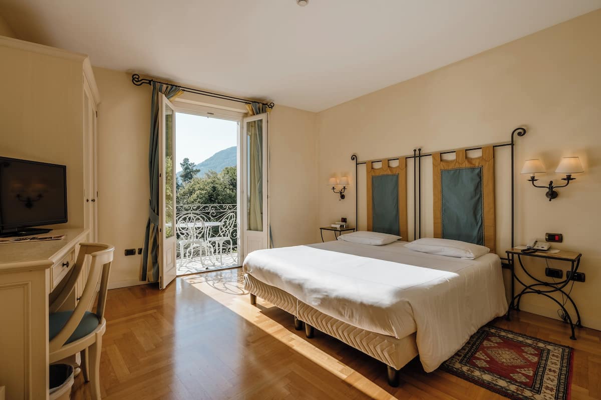 Une chambre à coucher avec un lit, des lampes de chevet, un bureau avec une télévision et une vue sur l’extérieur.