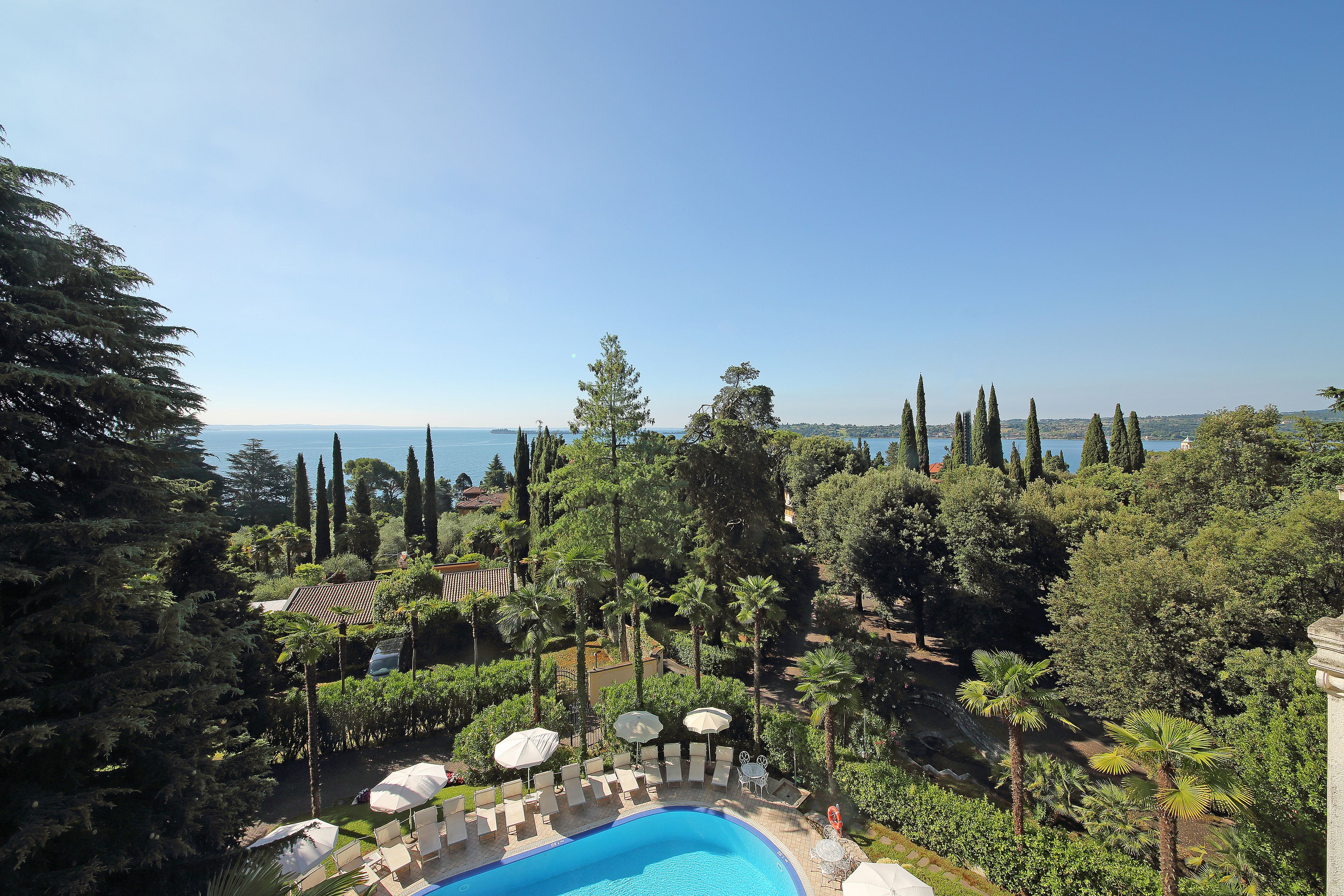 A pool area with lounge chairs and umbrellas, surrounded by trees and overlooking a body of water.