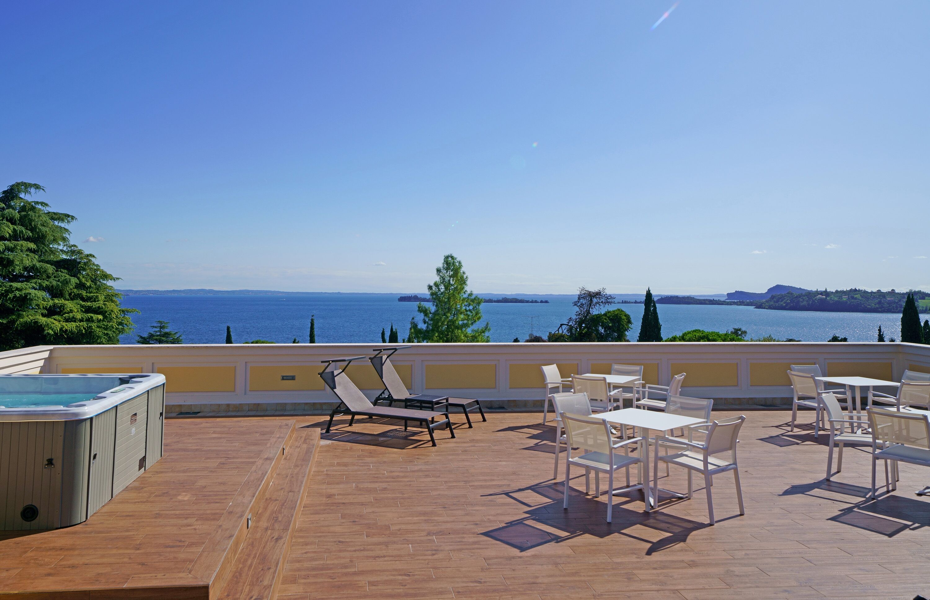 A terrace with a hot tub, lounge chairs, and dining tables overlooking a body of water.