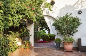 A patio area with potted plants, a white curtain, and a wicker chair.