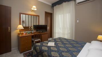 Habitación de hotel con cama, escritorio con televisor, cómoda y ventana con cortinas.