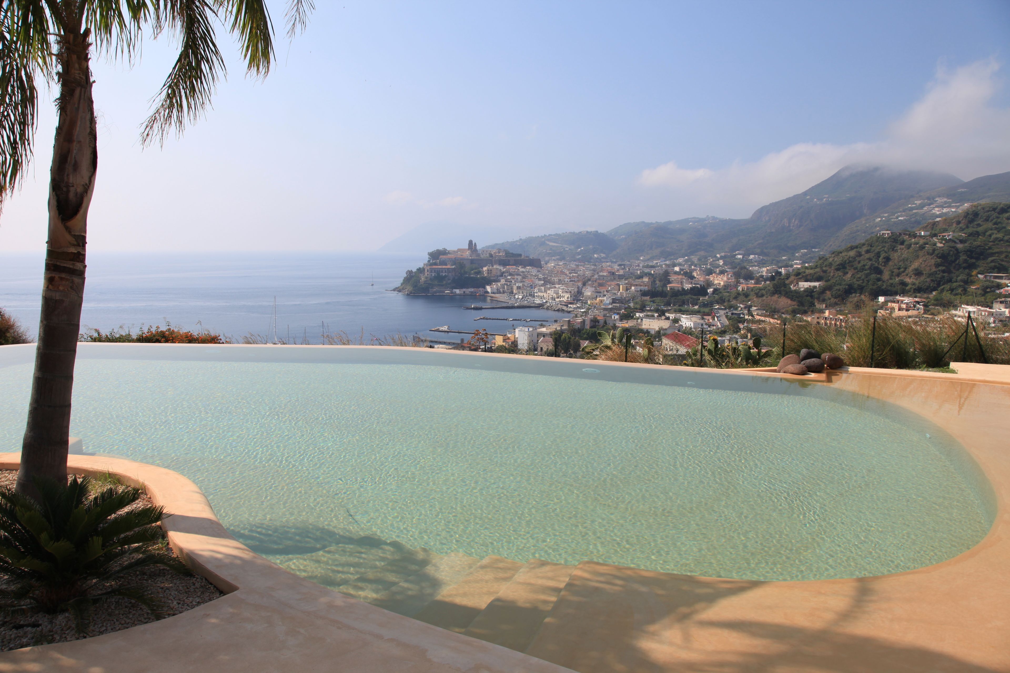 A clear swimming pool with a view of a coastal town and mountains in the background.