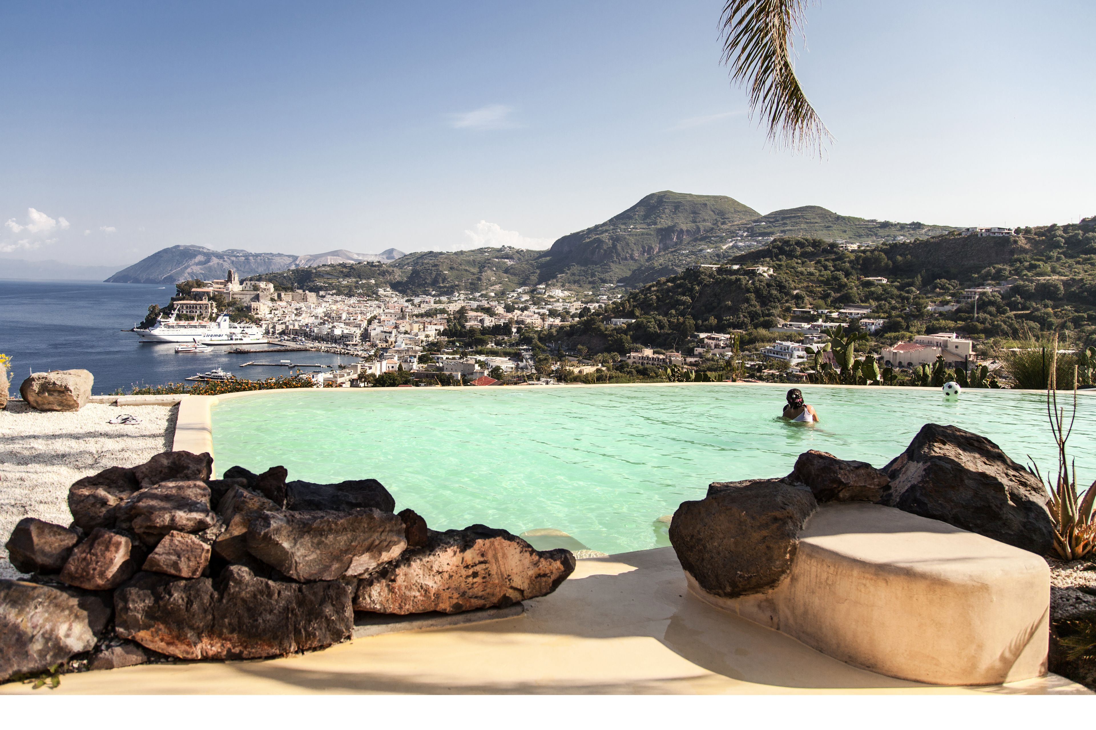 A pool with rocks and a view of a coastal town and mountains.