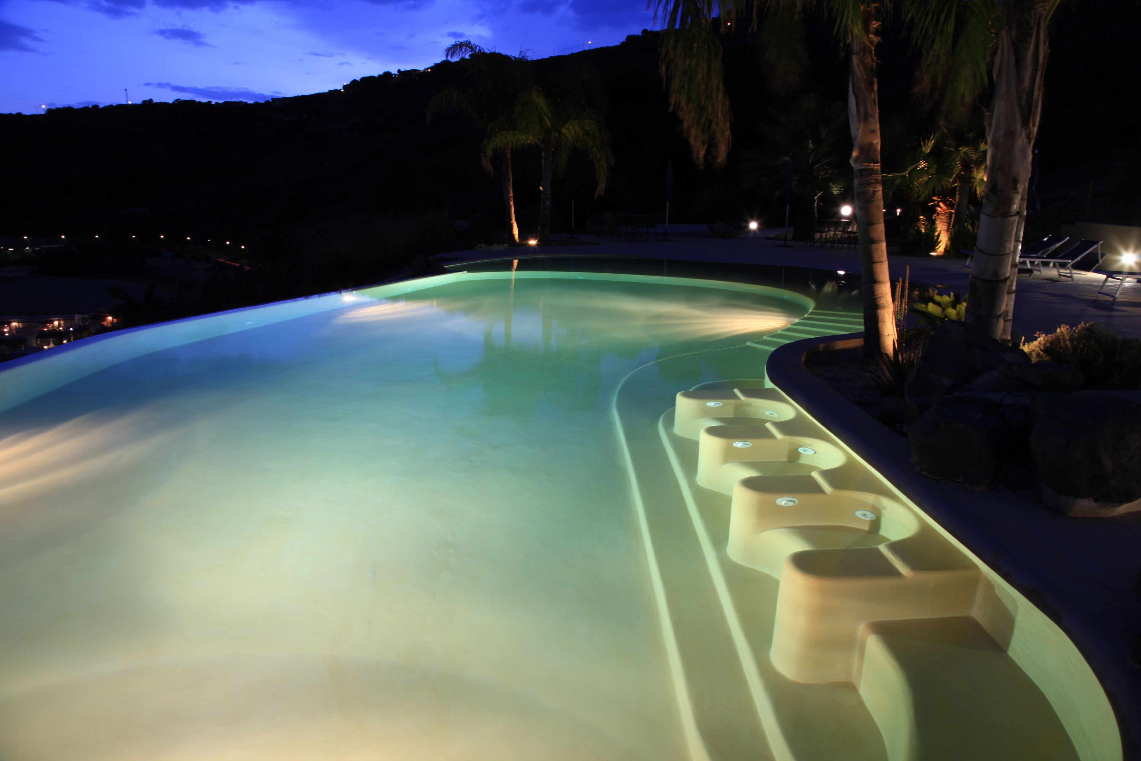 A swimming pool with a curved edge, surrounded by palm trees and a night sky.