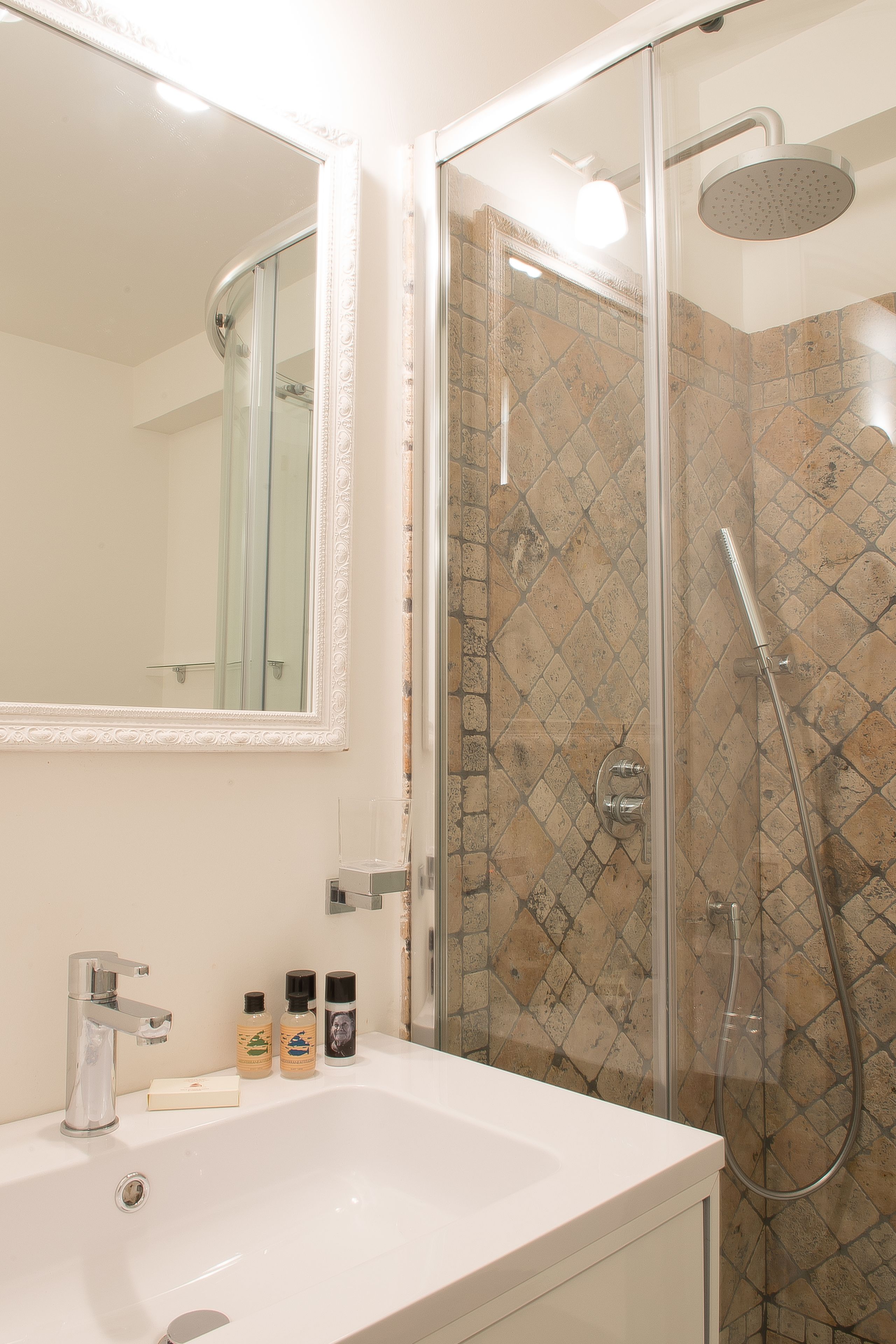 Un baño con lavamanos blanco, ducha envuelta en vidrio y pared con azulejos.