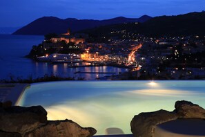 A nighttime view of a coastal town with a lit-up harbor, a large building on a hill, and a clear sky. - Hotel Villa Enrica - Aeolian Charme (Lipari)
