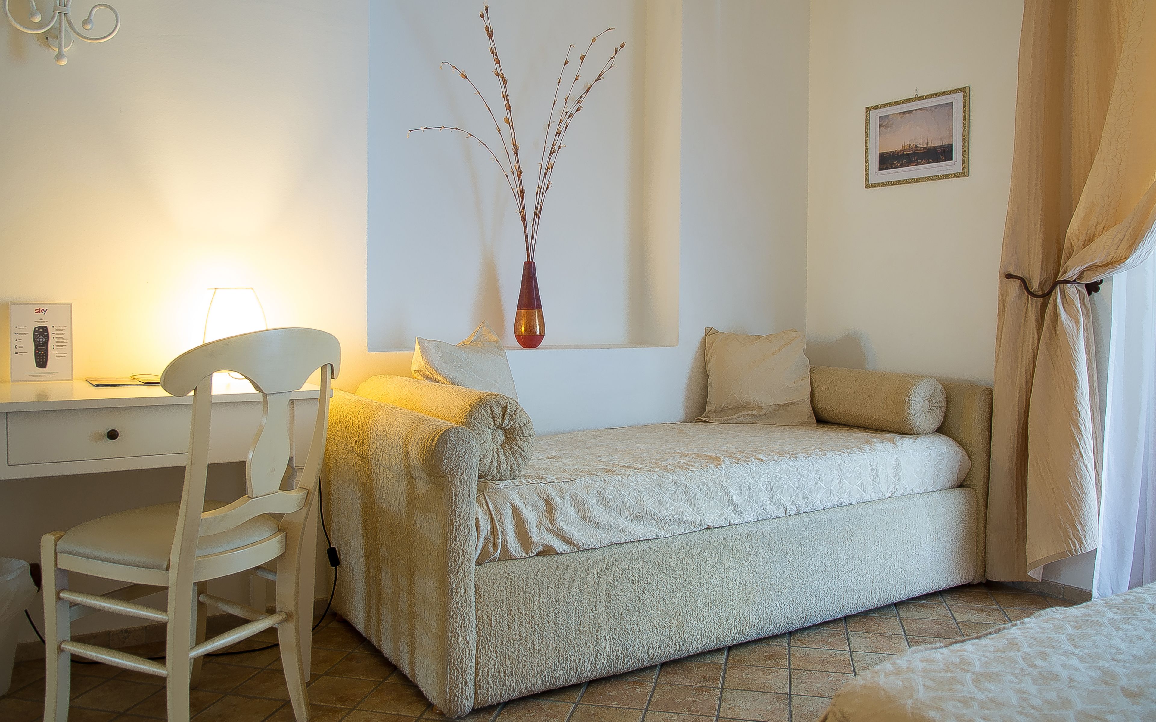 Ein Schlafzimmer mit Bett, Schreibtisch, Stuhl, einer Vase und einem Bild an der Wand.