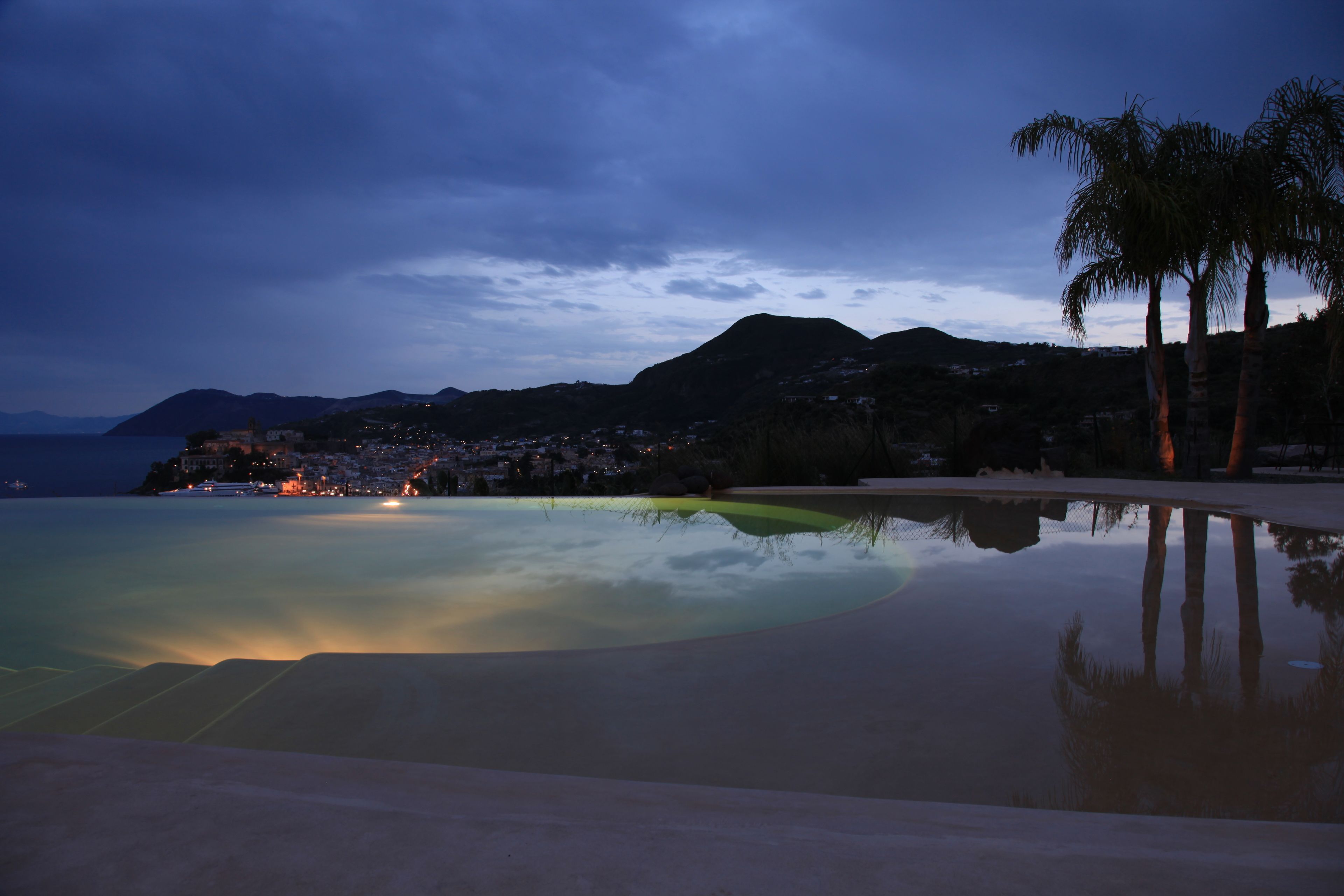 Una playa tranquila con una piscina cristalina que refleja el cielo y palmeras.