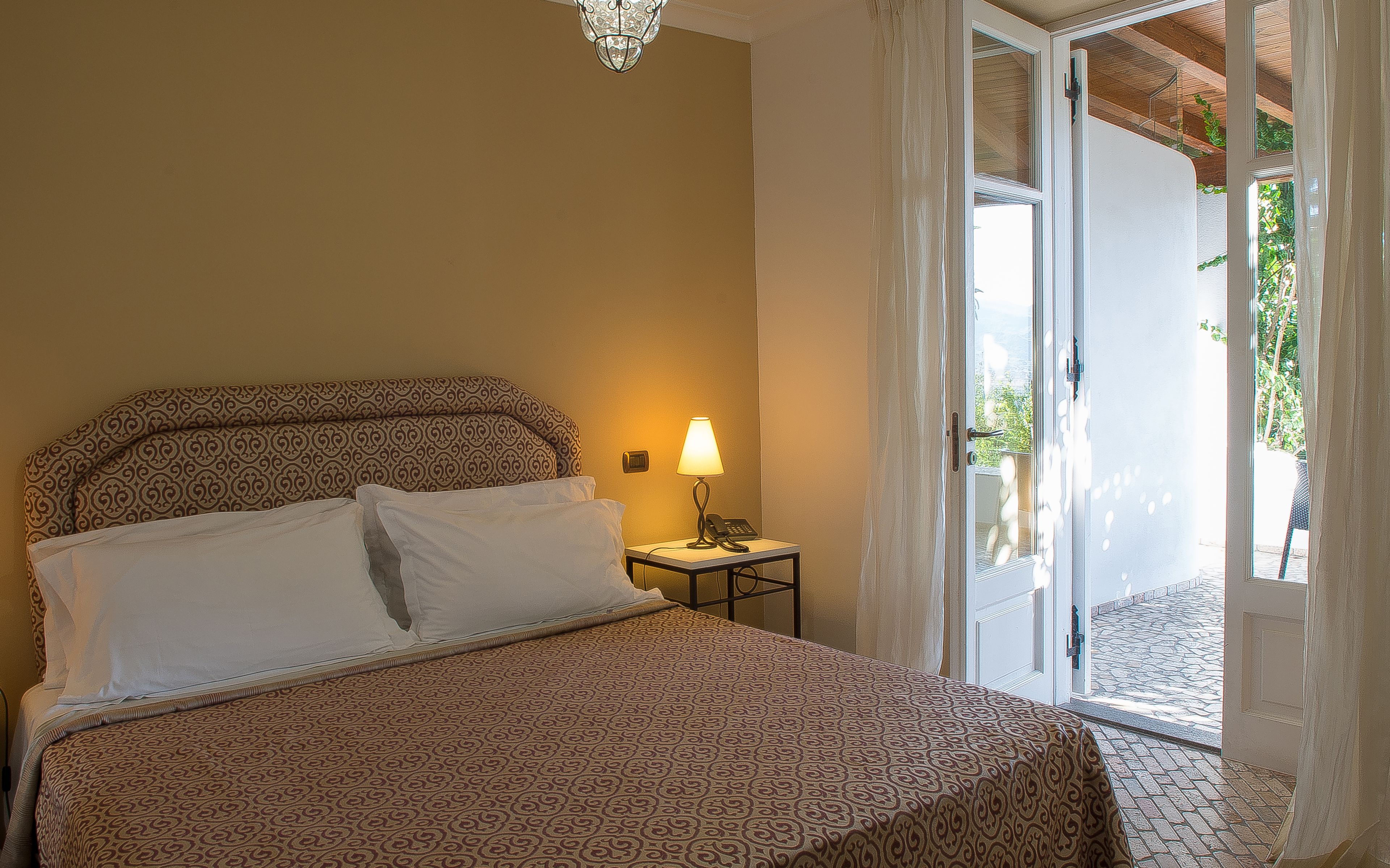 A hotel room with a bed, a bedside lamp, and a view of the outside.