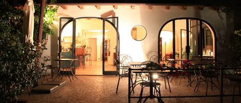 An outdoor patio area with tables and chairs, a dining area with a table and chairs, and a large arched doorway leading to an interior space.