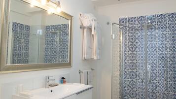 A bathroom with a white sink, a mirror with lights, a shower with blue patterned tiles, and a towel rack with towels.