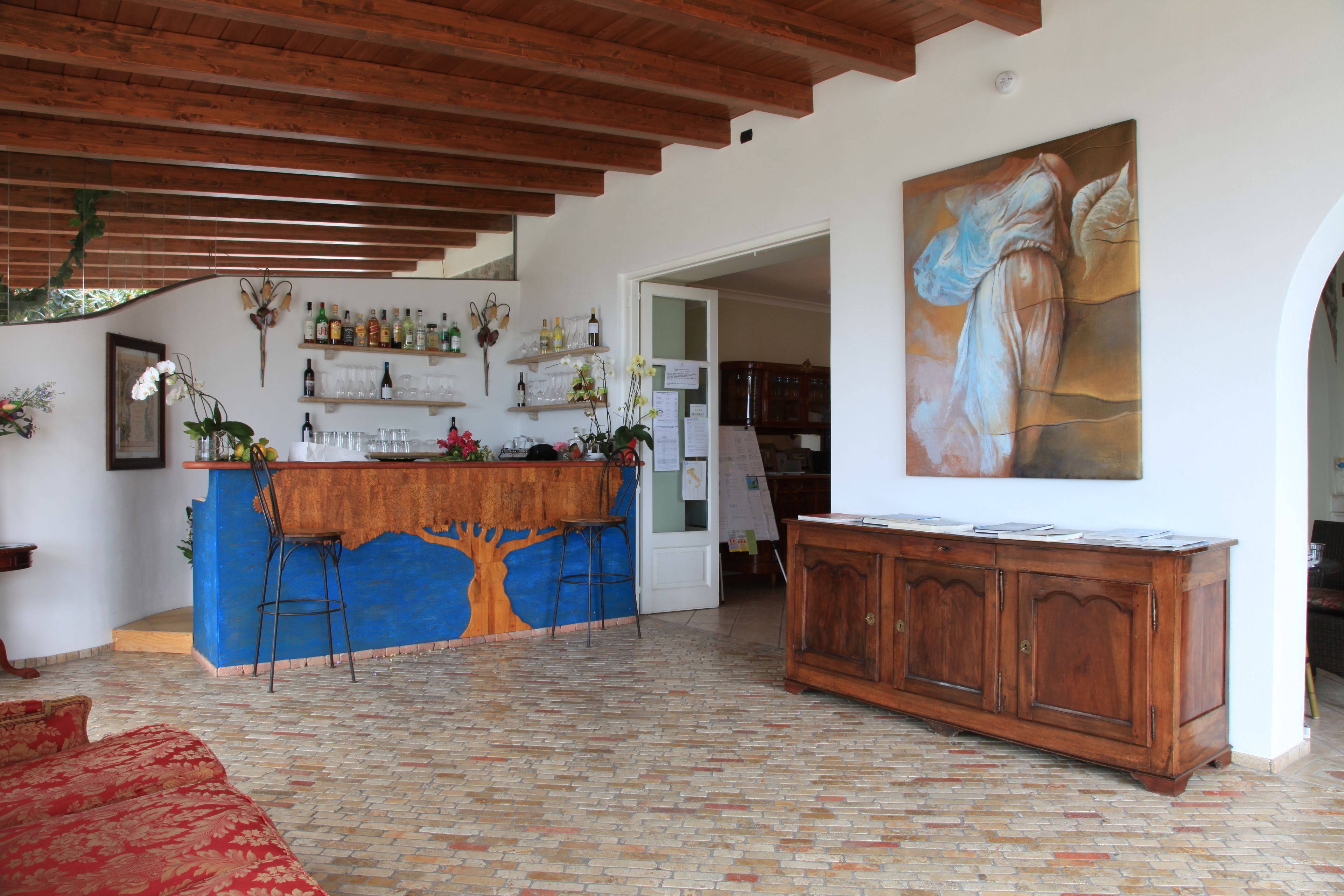 A spacious room with a wooden ceiling, a blue bar area, a wooden cabinet, and a large painting on the wall.