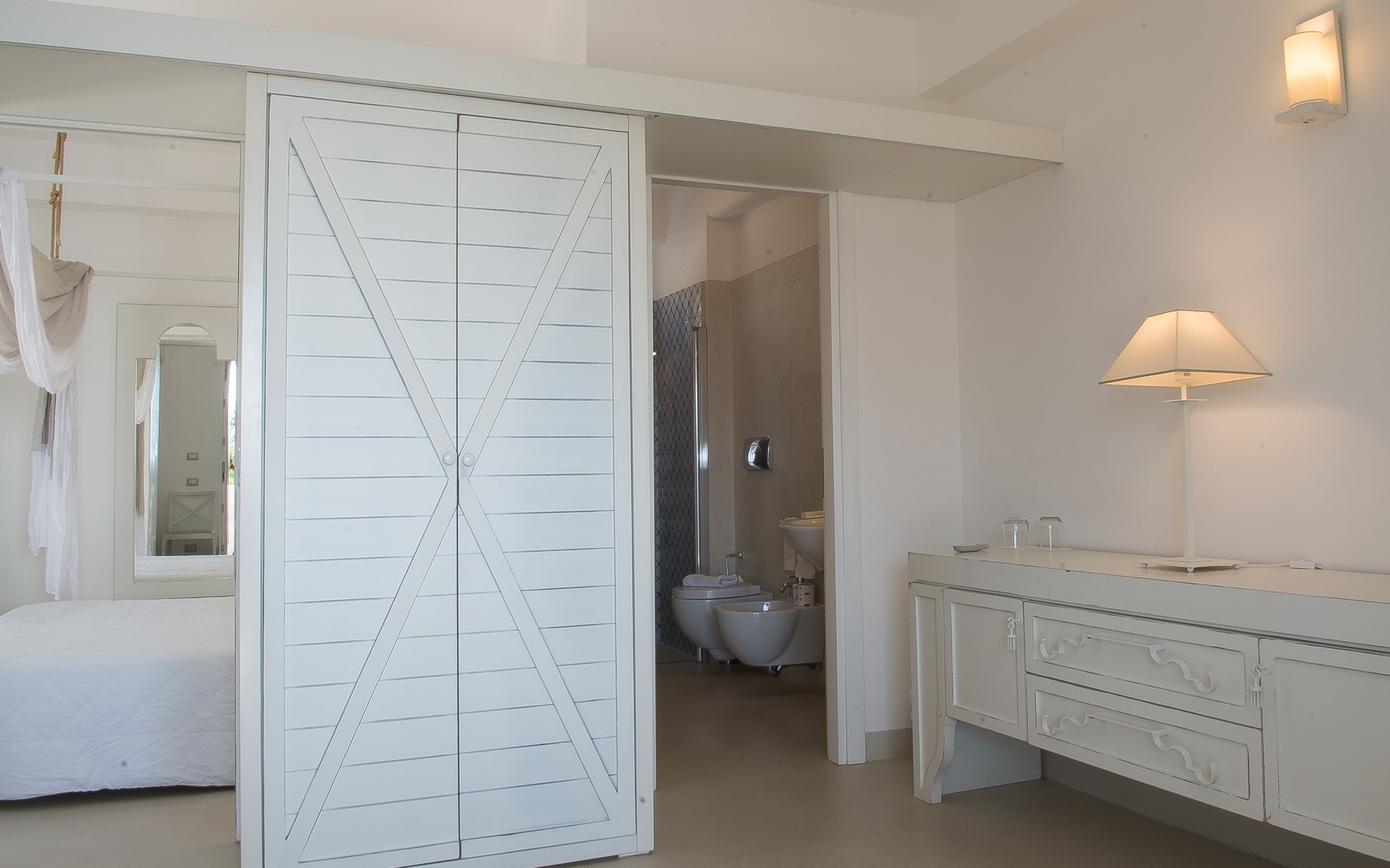 A bedroom with a large wardrobe, a bedside table, and a lamp.