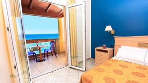 A hotel room with a bed, a nightstand, a table with chairs, and a view of the ocean through a sliding glass door.