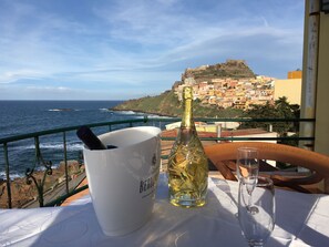 A table with a bottle of champagne, a glass, and a bucket, overlooking the sea and a coastal town. - Nadir (Castelsardo)