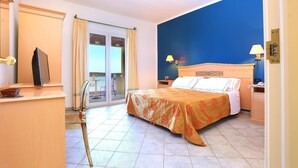 A hotel room with a bed, a desk with a computer, a chair, and a balcony with a view.
