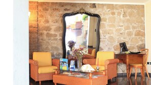 A living room with wicker furniture, a glass coffee table, and a large mirror on a stone wall.