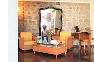 A living room with wicker furniture, a glass coffee table, and a large mirror on a stone wall.