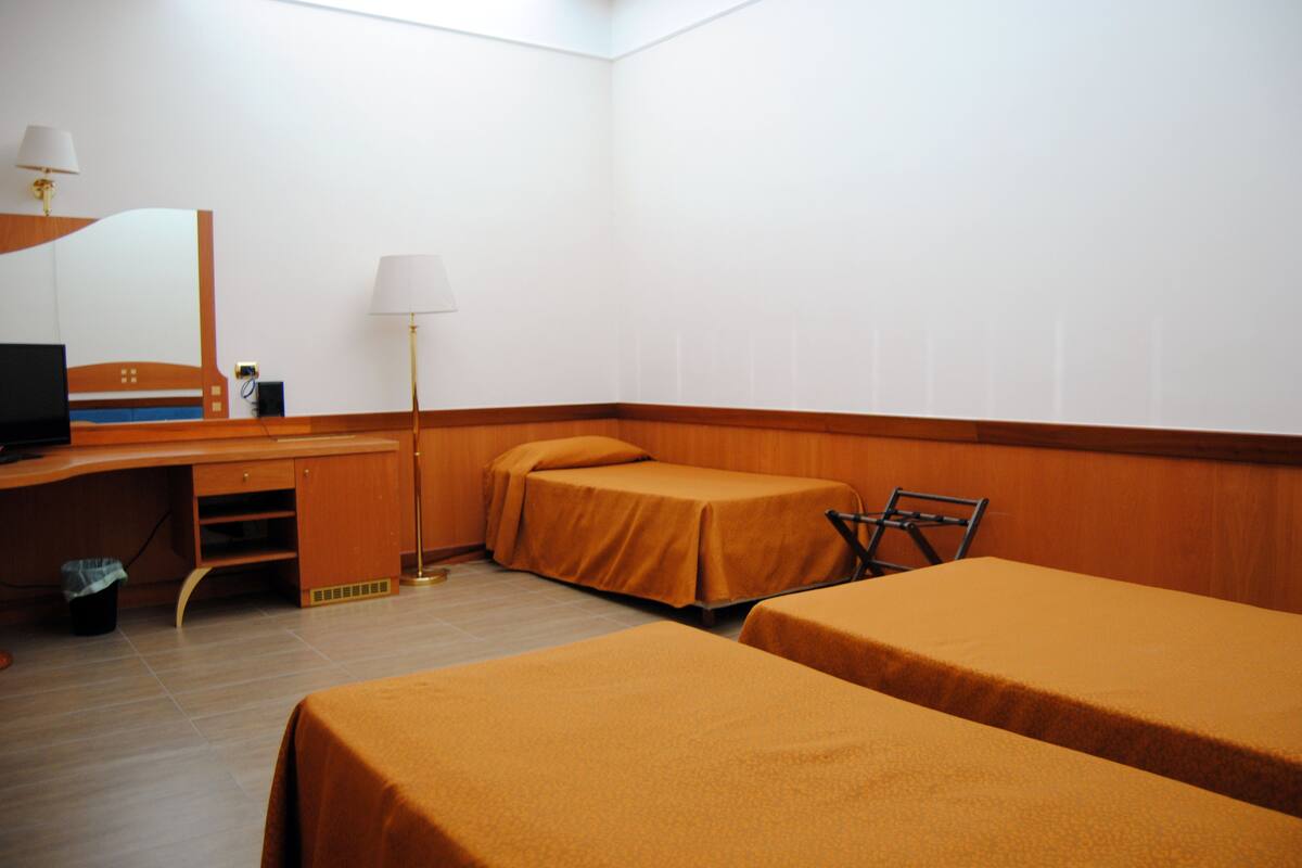 A hotel room with two single beds, a desk with a computer, a lamp, and a chair.
