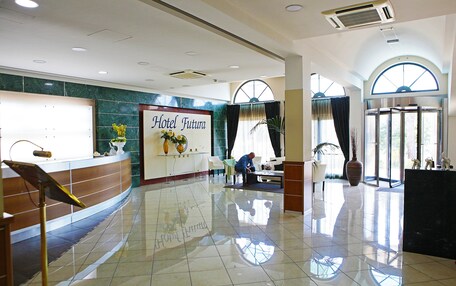 A hotel reception area with a polished floor, a reception desk, a large window, and a sign that reads "Hotel Futura".