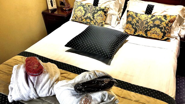 A neatly made hotel bed with a black and gold patterned pillow, a black pillow with a dotted pattern, and a red item on the bed. - Hotel Villa Savoia (Turin)