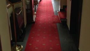 A hotel corridor with a red carpet, a sign indicating breakfast hours, and a door leading to a room. - Hotel Villa Savoia (Turin)