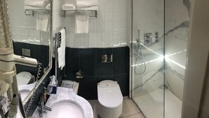 A modern bathroom with a marble sink, a toilet, a glass-enclosed shower, and a vanity with a mirror and towel rack. - Hotel Villa Savoia (Turin)