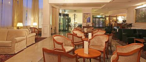 A hotel lobby with a seating area, a reception desk, and a view of the outside through a glass door.