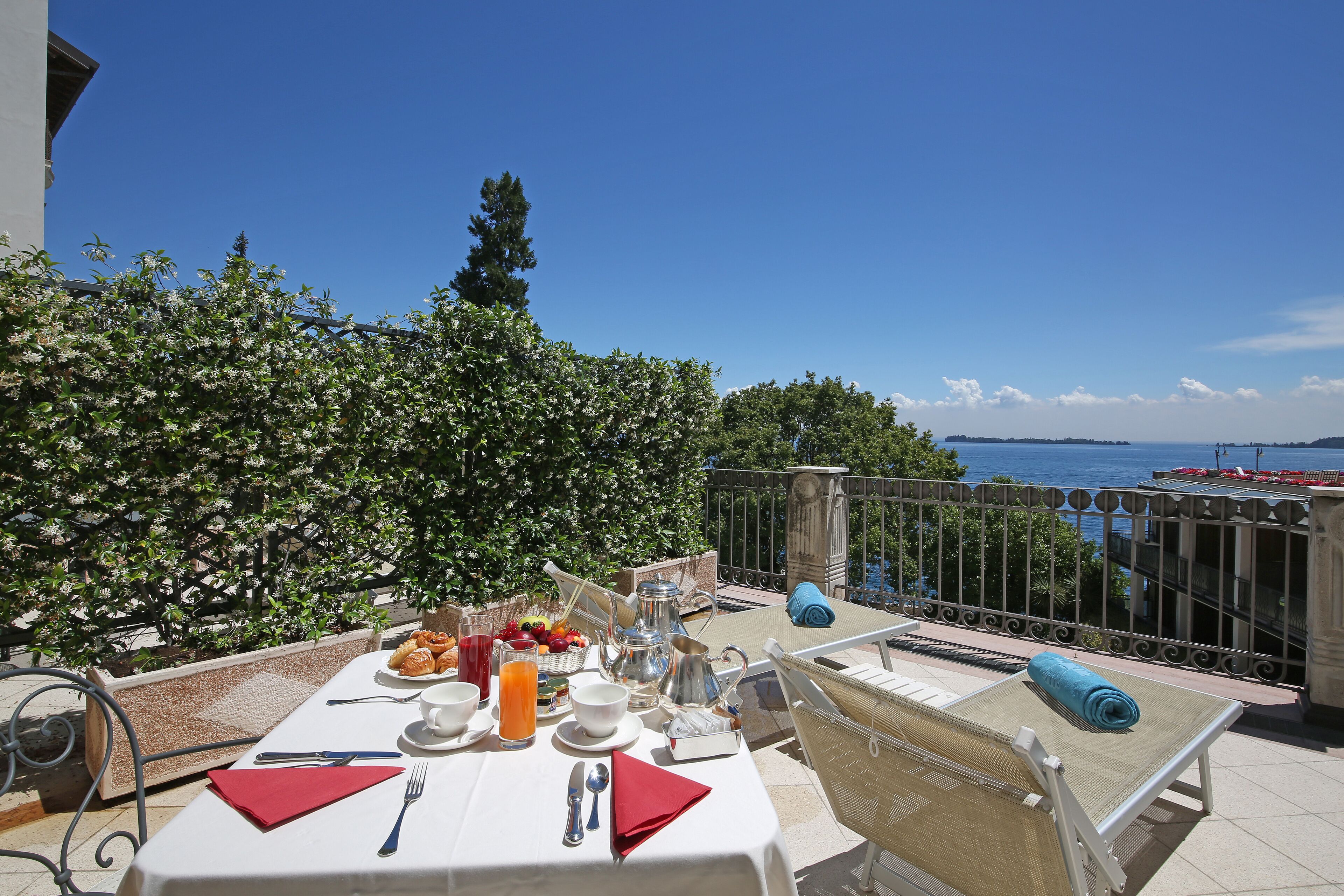 Mesa lista para el desayuno con vista al mar, una barandilla de metal y una toalla azul en una silla.